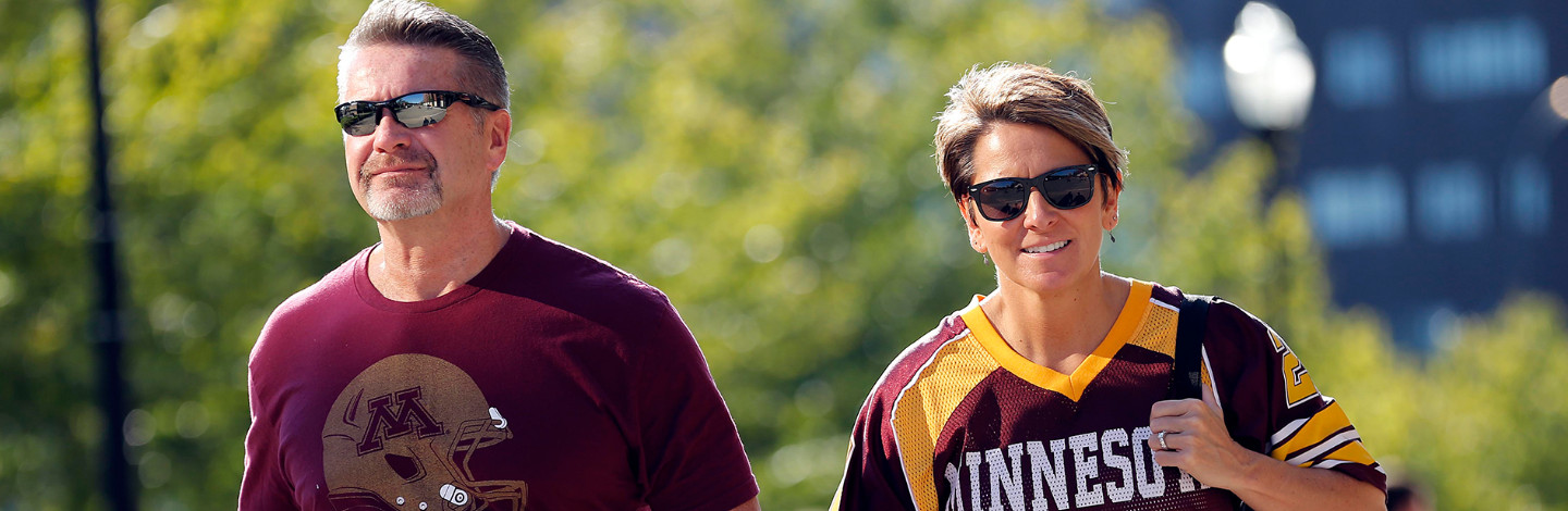Two parents wearing gopher gear walk on campus