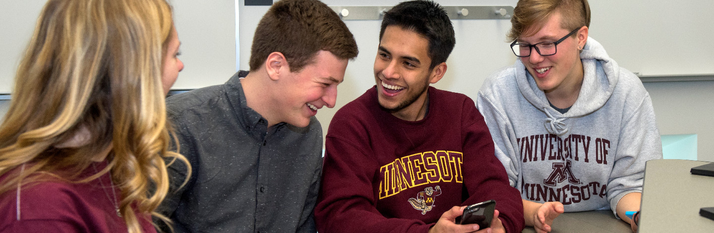 Students wearing gopher gear laugh while looking at a cell phone