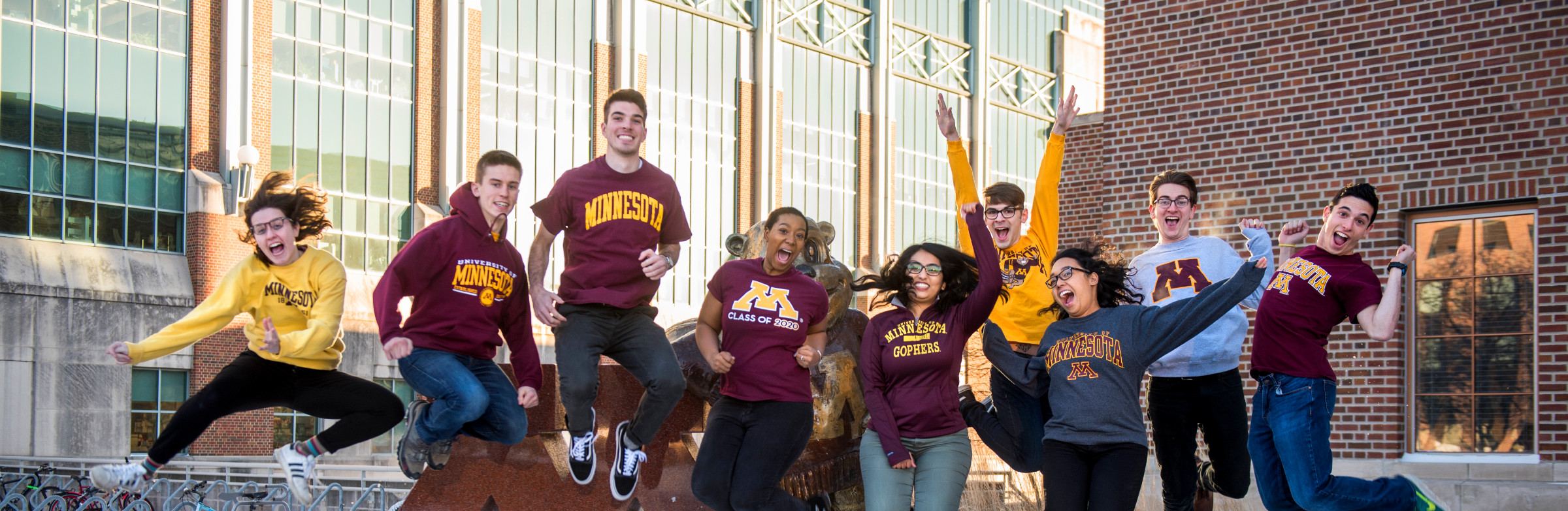 Students jump in the air in front of a snow covered Goldy and Block M statue