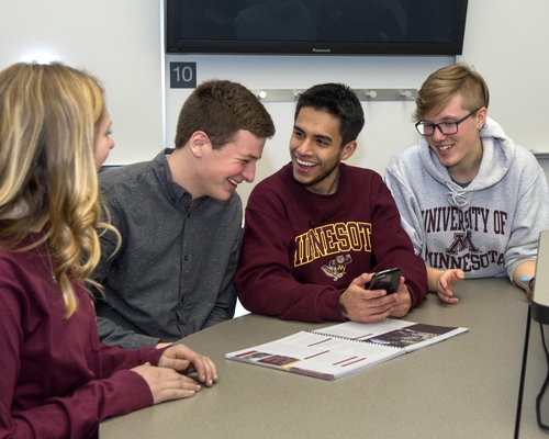 Students wearing gopher gear laugh while looking at a cell phone