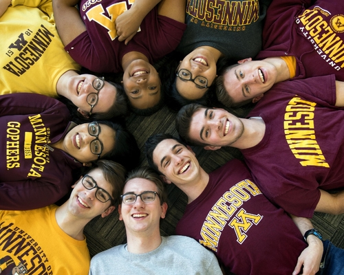 Students wearing Gopher gear lay on their backs in a circle with their heads touching